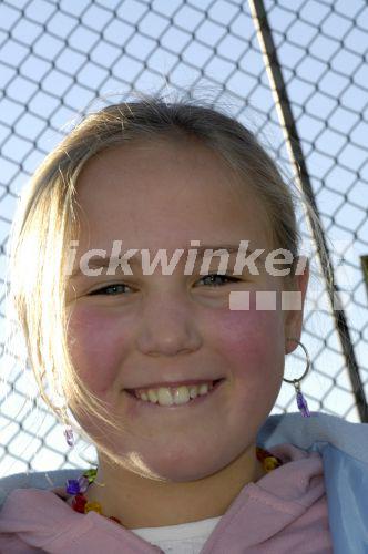 young girl smiling in front of a chain-link fence